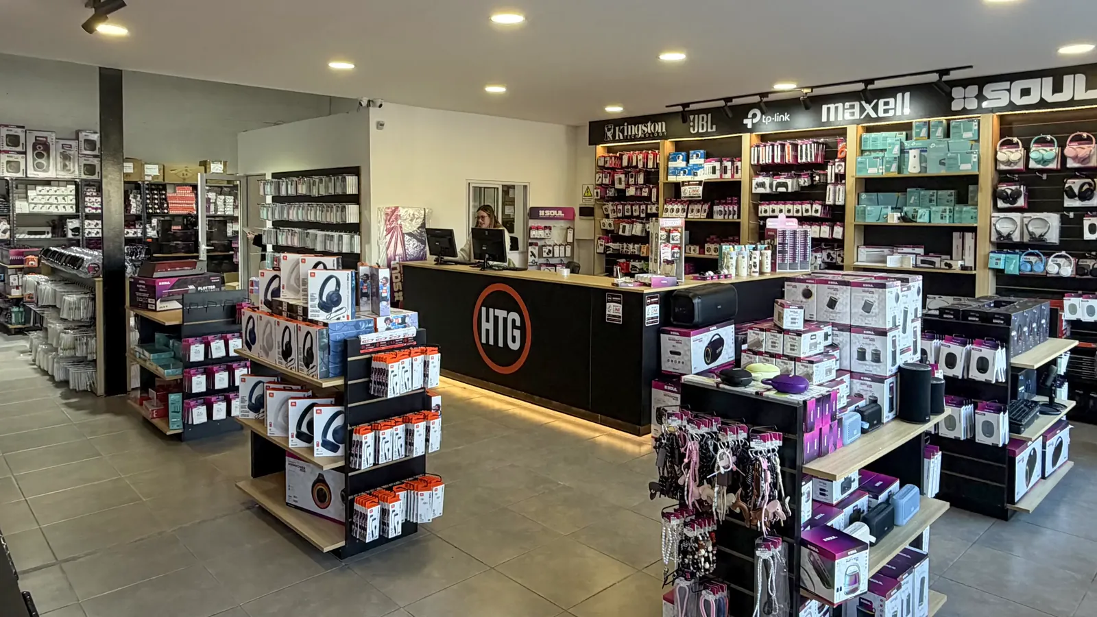 Sal&oacute;n mayorista de HTG: el mostrador con el logo y la pared de marcas Kingston, JBL, TP-Link, Maxell y SOUL